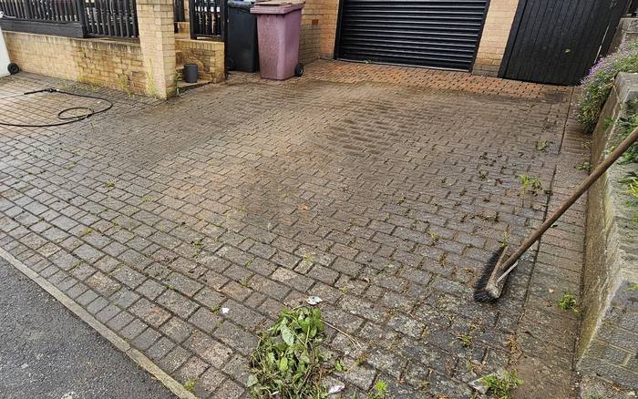 Block paving driveway dulled with dirt and weeds growing through the joints