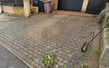 Block paving driveway dulled with dirt and weeds growing through the joints