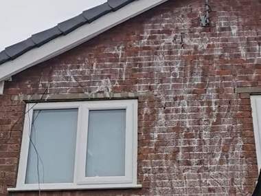 A brick gable part way through a soft wash treatment