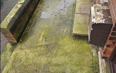 Concrete forecourt covered in thick green algae before pressure washing