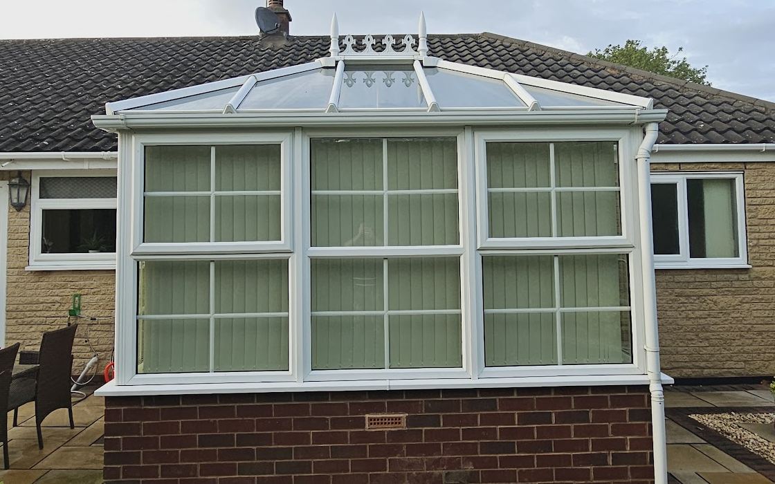 A conservatory with a glass roof and frames cleaned back to white