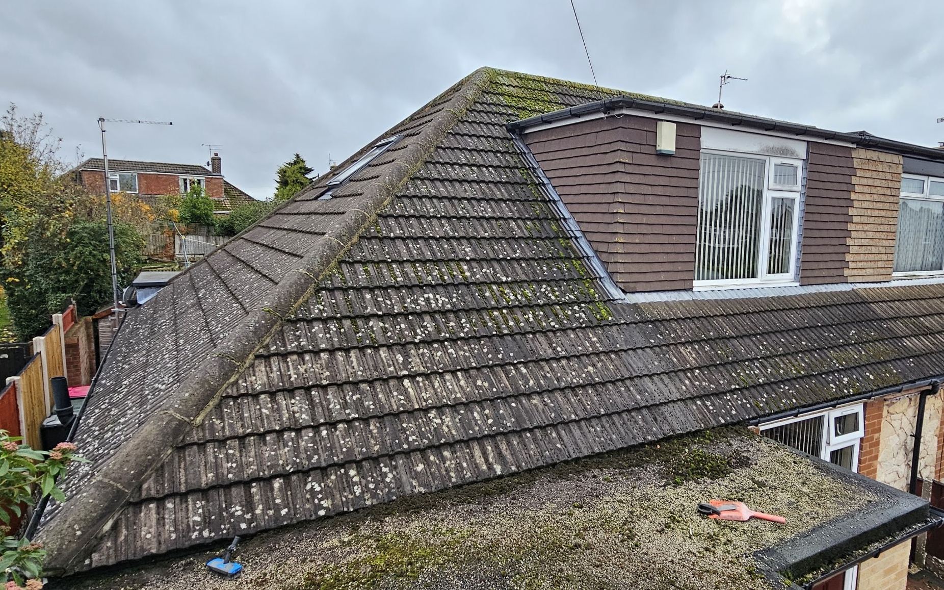 A large hipped roof covered in moss and lichen before cleaning