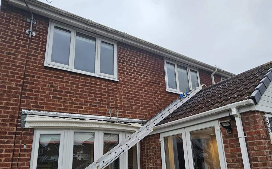 Ladder and pole system set up against a house for gutter and roofline work