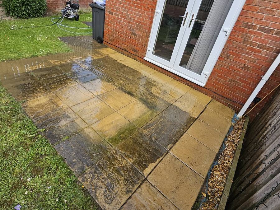 Indian sandstone patio part way through being pressure washed, with the machine running