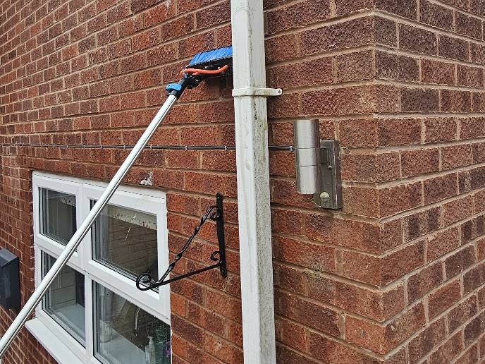 The brush head on a pole working across brickwork